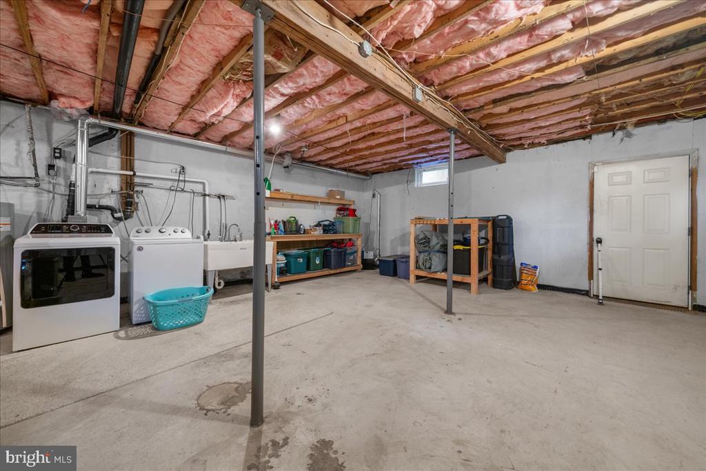 Unfinished basement laundry area with washer, dryer, storage shelves, and exposed insulated ceiling.