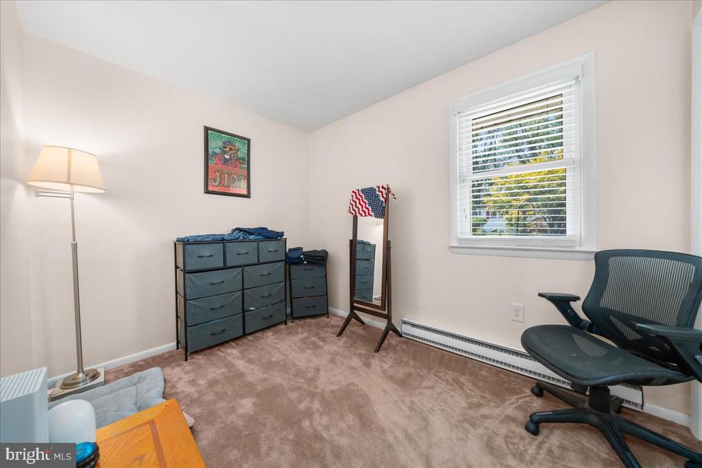Furnished room with brown carpet, fabric drawer units, a standing mirror, and a rolling office chair.
