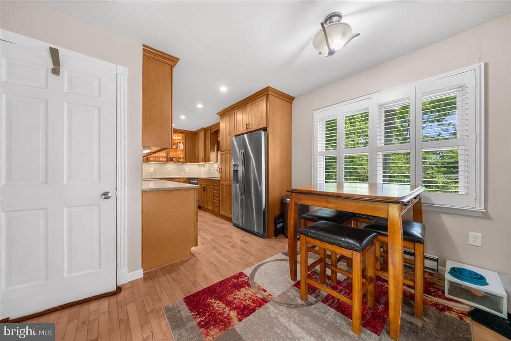 Kitchen and dining area with warm wood cabinets, stainless steel refrigerator, and a table beside shuttered windows.