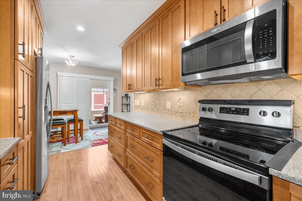 Kitchen with honey-toned wood cabinets, stainless steel appliances, and a dining area beyond.
