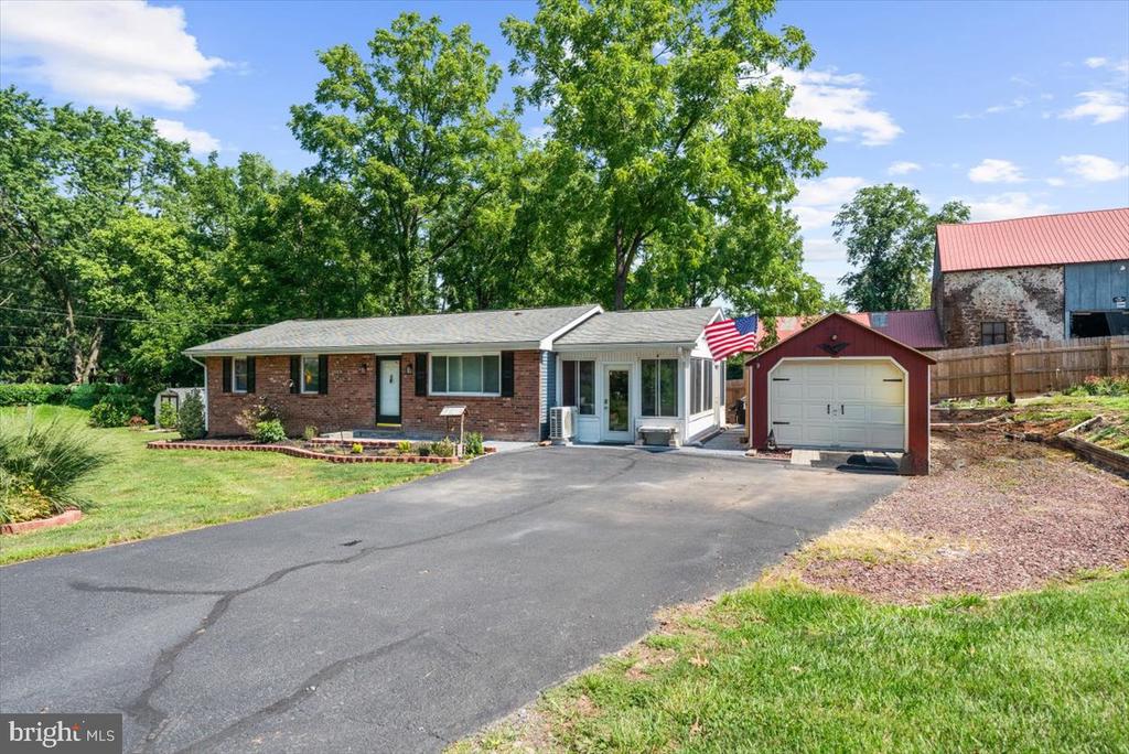 Brick ranch home with an enclosed sunroom, detached garage, and wide driveway.