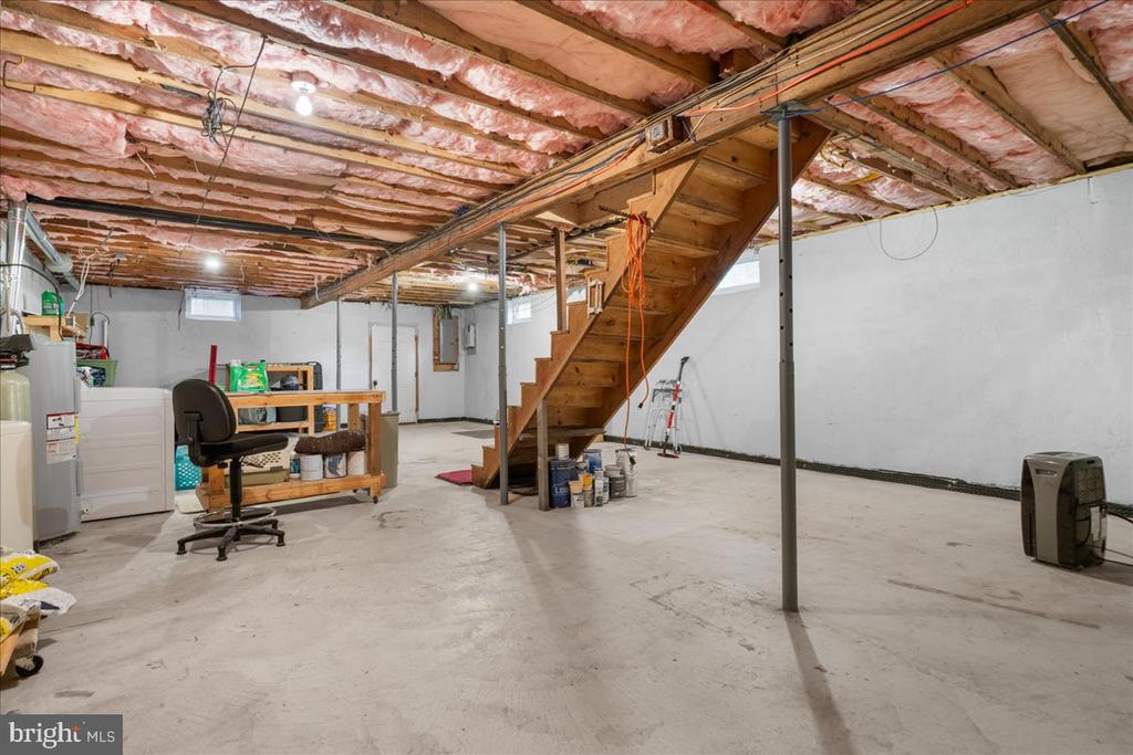 Unfinished basement with exposed ceiling insulation, support posts, and a wooden staircase.