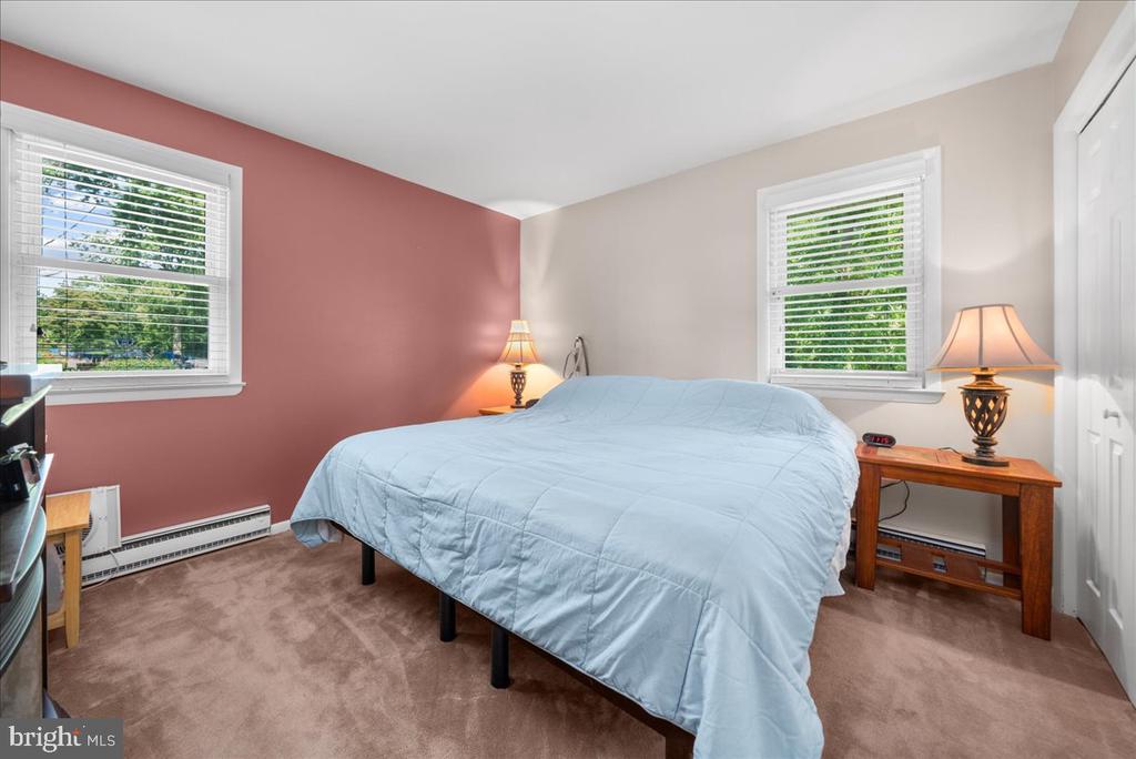 Bedroom with a light blue-covered bed, rose accent wall, and two windows with white blinds.