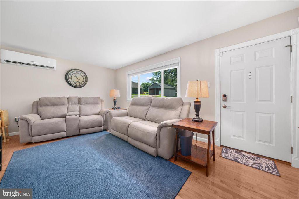 Living room with gray reclining sofas, a large blue rug, and a white entry door.