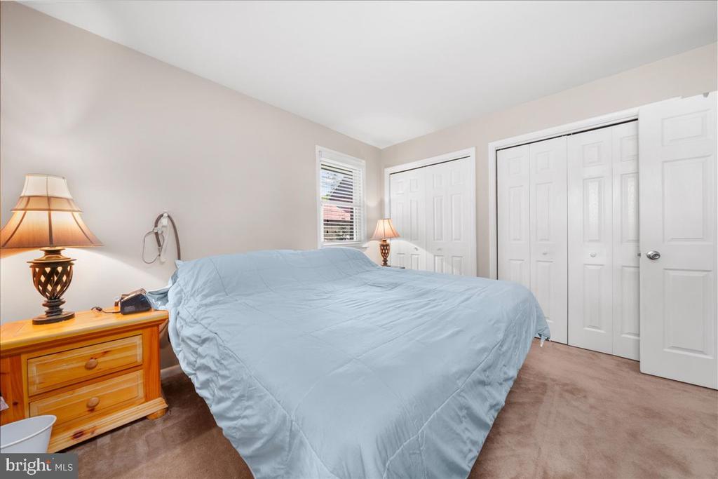 Bedroom with a large bed in light blue bedding, wooden nightstand, and white closet doors.