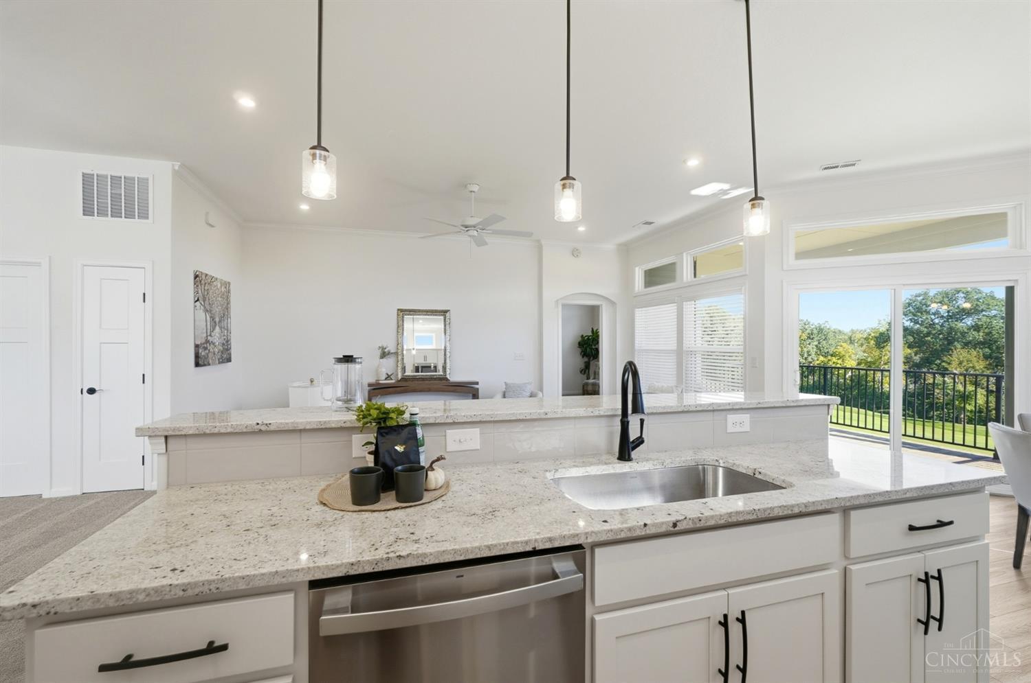 Bright kitchen with a granite island, black faucet, stainless-steel dishwasher, and windows overlooking leafy trees.