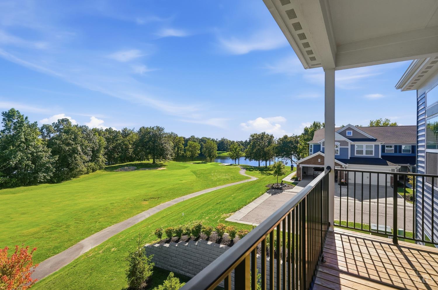Balcony overlooking a golf course and lake, with a winding path and neighboring homes.