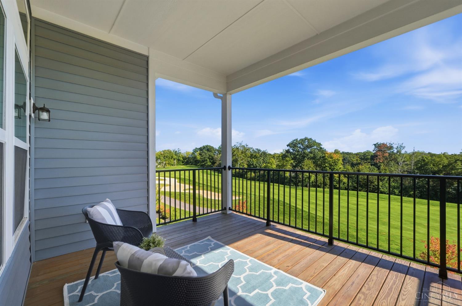 Covered deck with wicker seating overlooking a manicured lawn and tree line.
