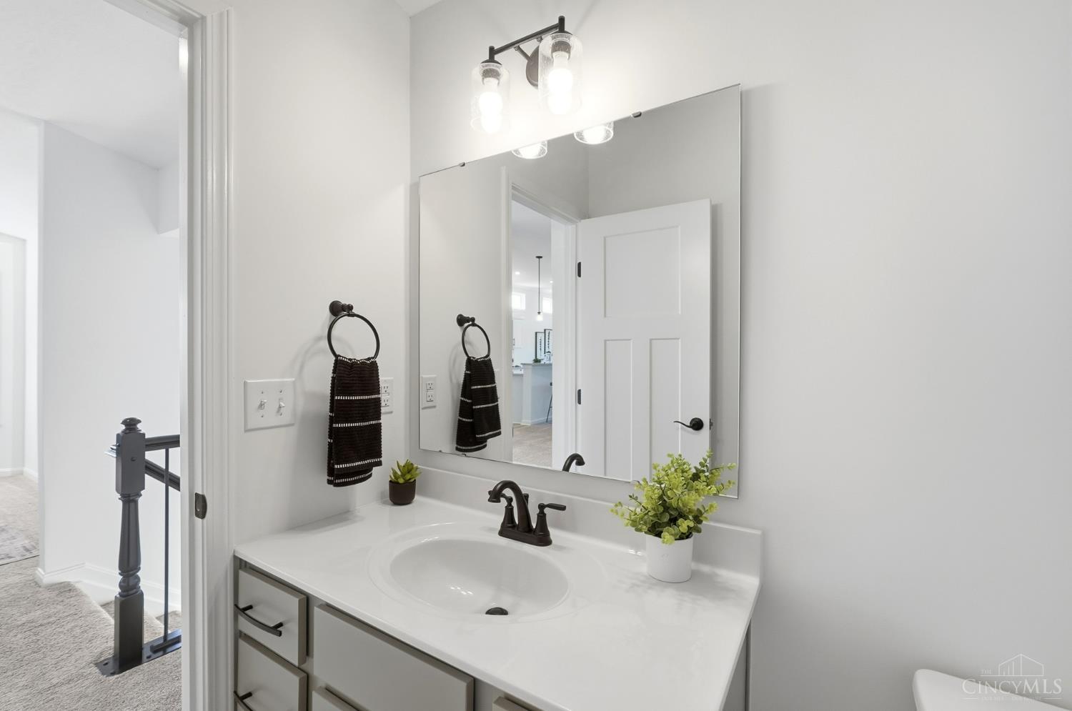 Bathroom vanity with an oval sink, large mirror, dark faucet, and potted plants.