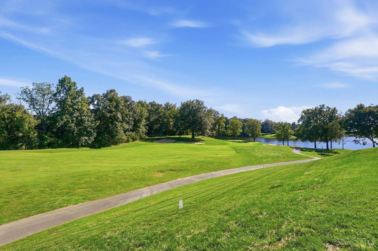 Golf course with a curving cart path, tree-lined fairway, and lake.