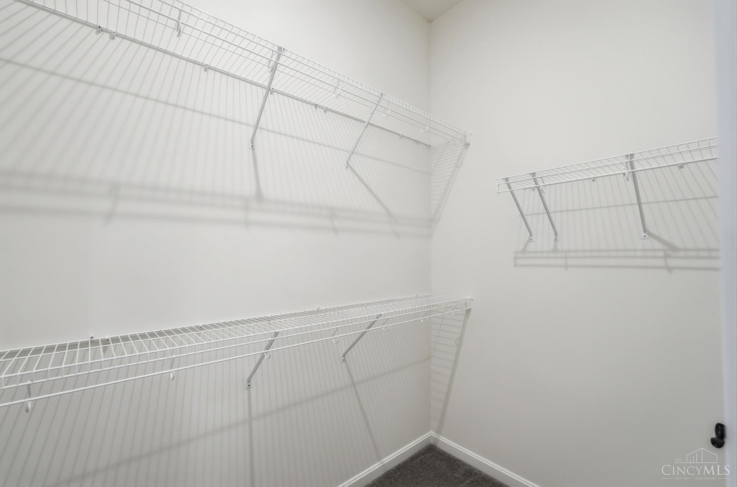 Walk-in closet with white wire shelving on three walls and gray carpet.