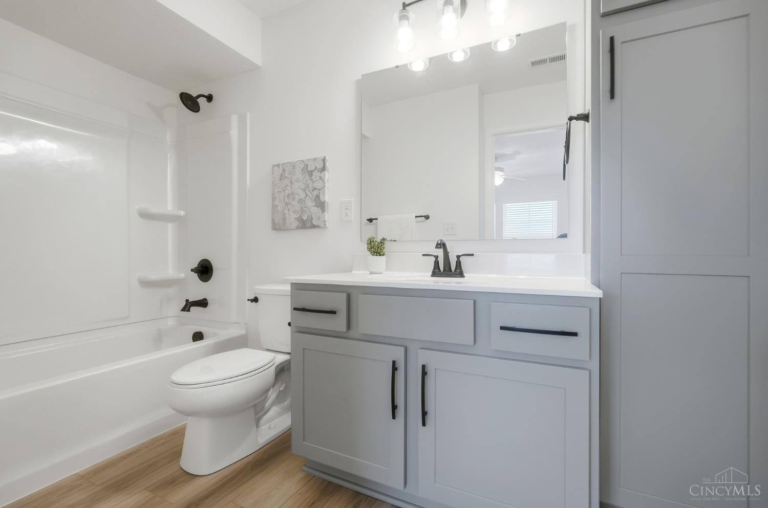 Bathroom with a gray vanity, large mirror, white tub and shower, and wood-look flooring.