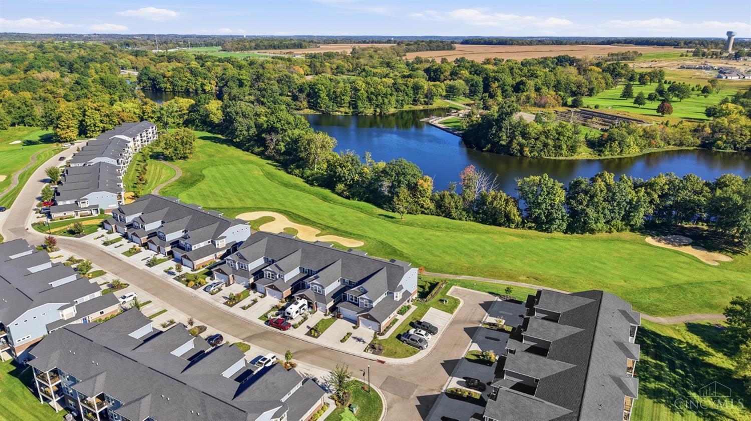 Aerial view of homes beside a pond and golf course, with green fairways and wooded surroundings.