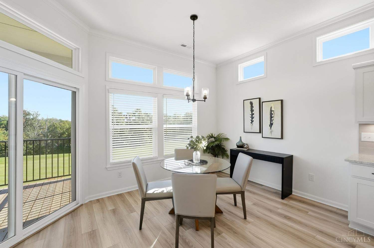 Dining area with a round glass table and tall windows overlooking a lawn, beside sliding doors to a deck.