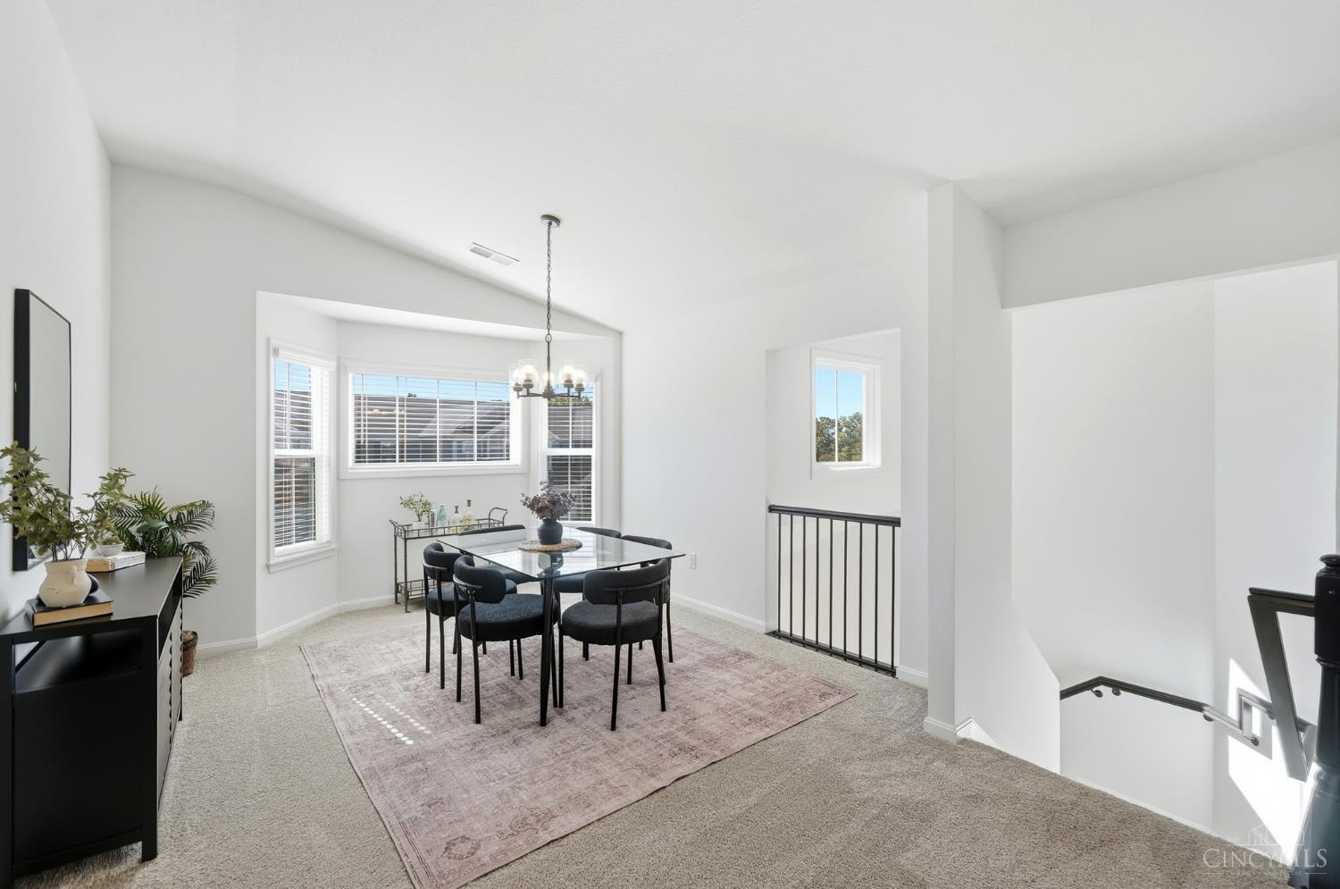 Bright dining area with a glass-top table, large blinded windows, and an open staircase.