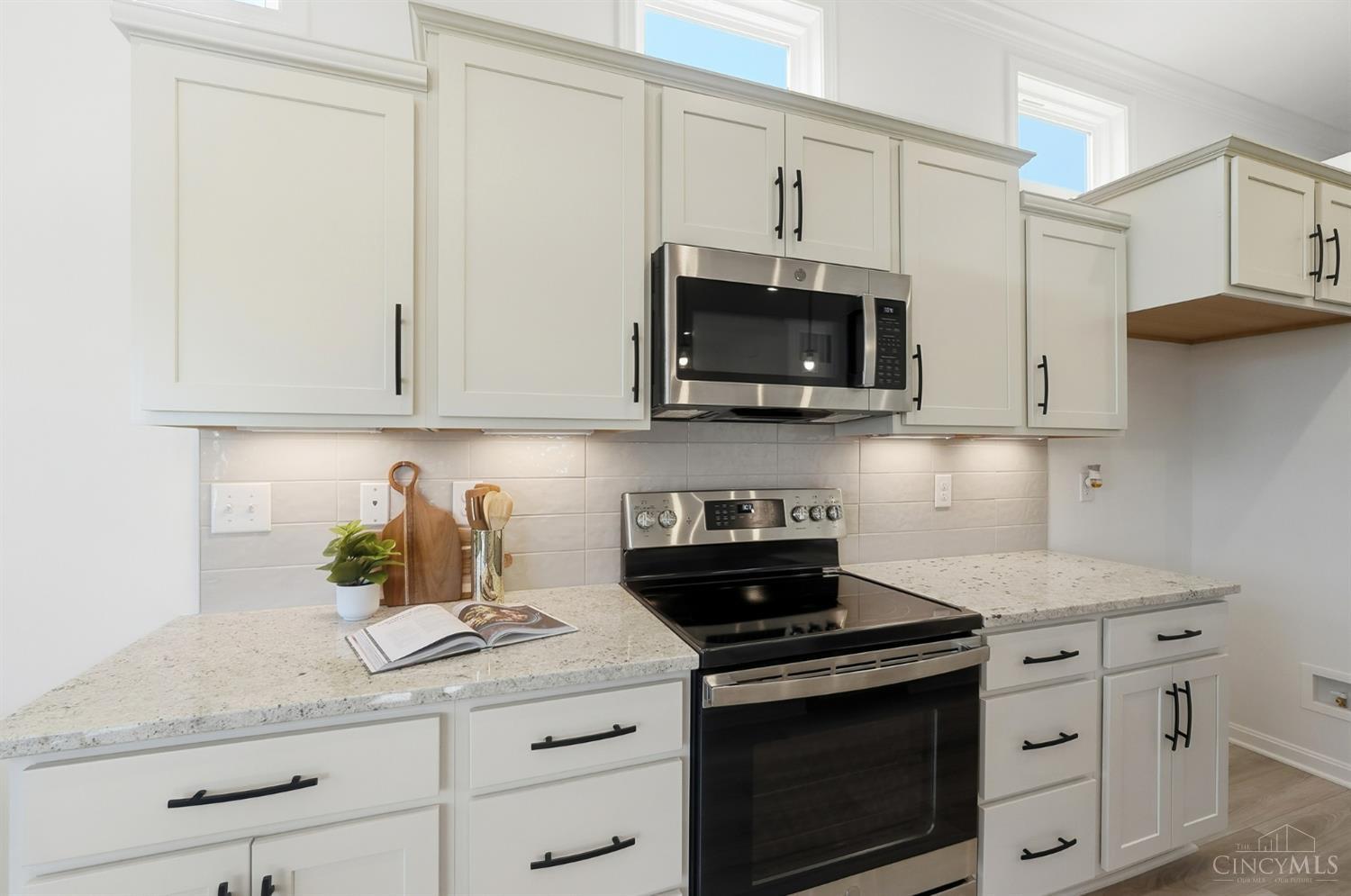 Kitchen with white cabinets, speckled granite counters, and a stainless steel microwave over a black range.