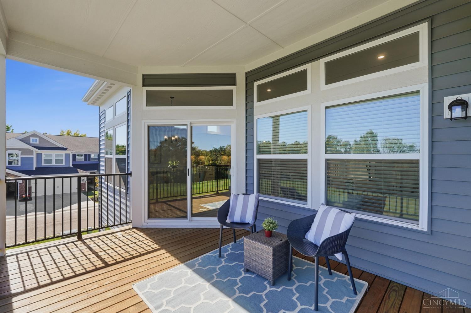 Covered deck with two chairs and a blue-and-white rug beside sliding glass doors.