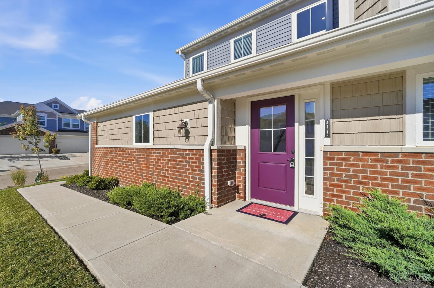 Home entrance with a purple front door, brick facade, and concrete walkway.