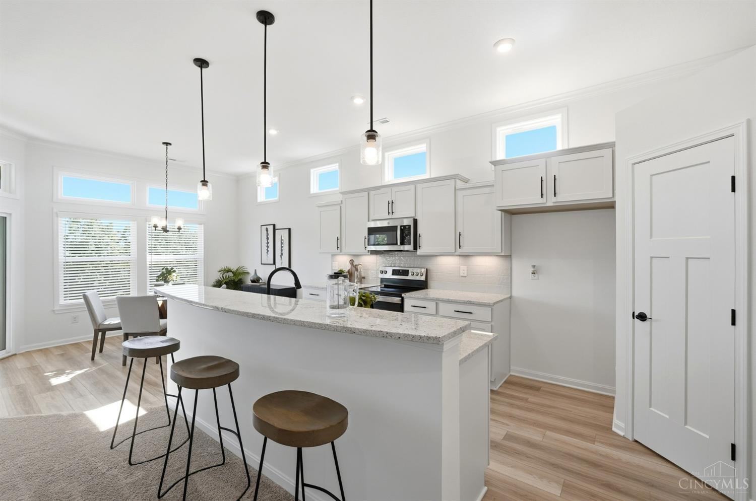 Bright white kitchen with a large granite island, bar stools, pendant lights, and a window-side dining nook.