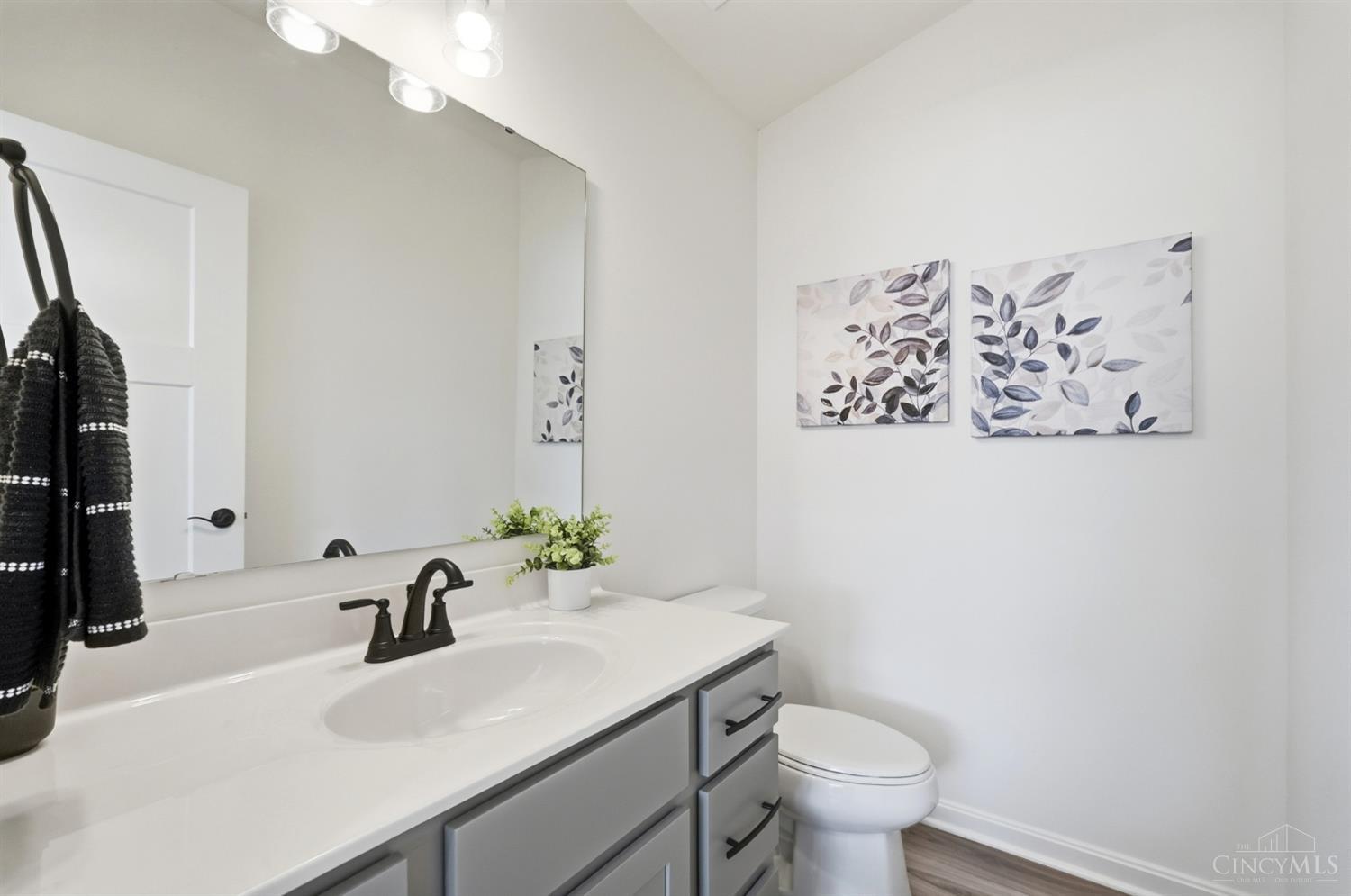 Bathroom with a gray vanity, white countertop, large mirror, and botanical wall art.