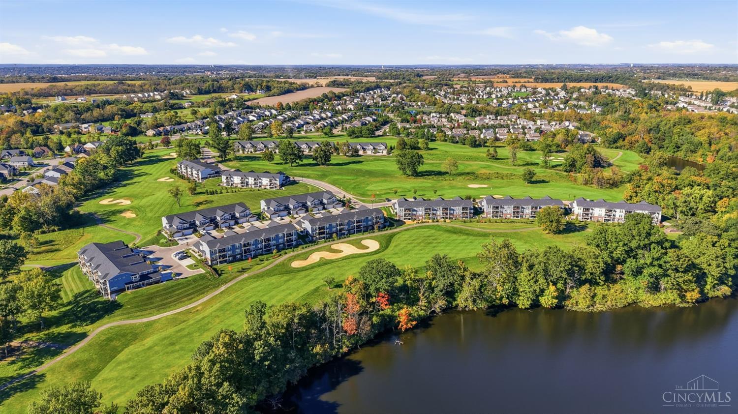 Aerial view of a golf course community beside a lake, with residences and autumn trees.