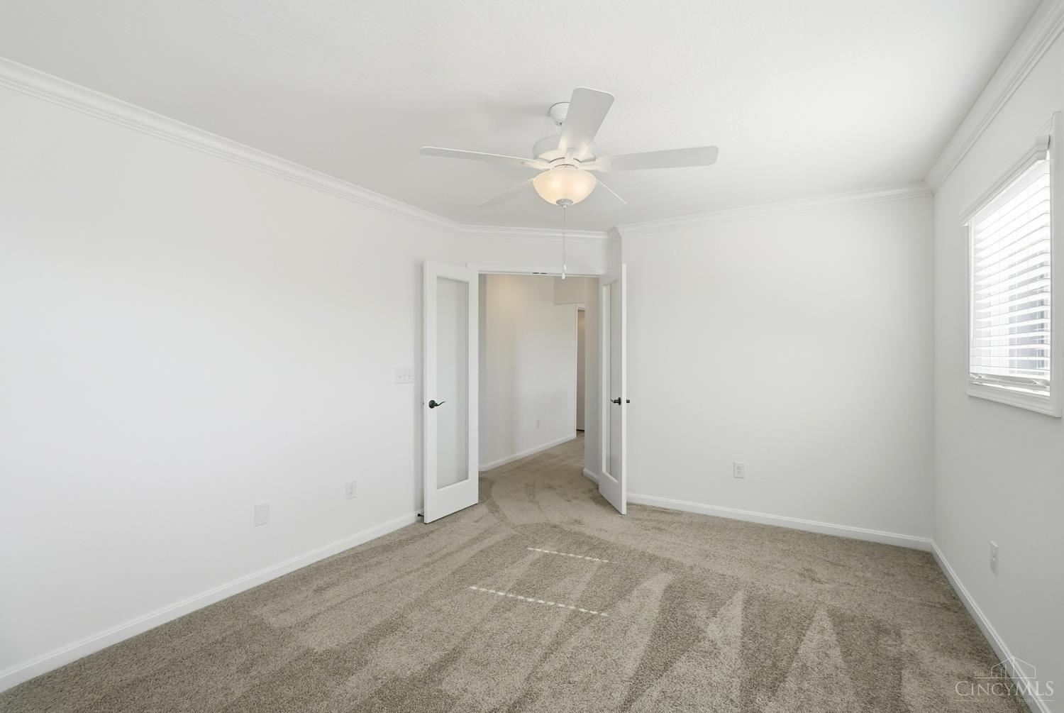 Unfurnished bedroom with beige carpet, a ceiling fan, and open double doors to a hallway.