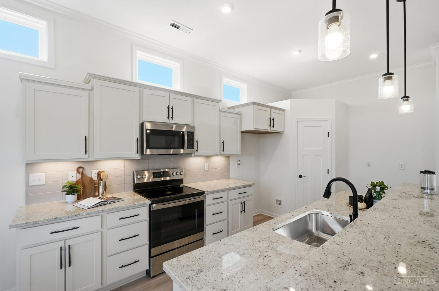 Bright kitchen with white cabinets, stainless appliances, and a granite island with an undermount sink.