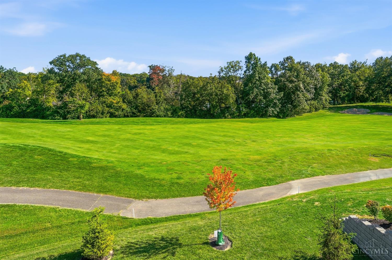 Golf course fairway with a curving path, mature trees, and a small sand bunker.