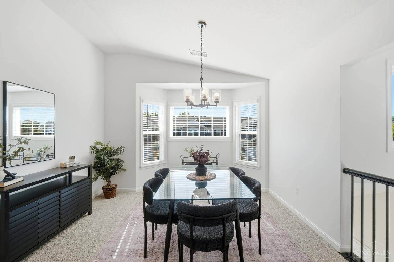 Bright dining room with a glass-top table, dark chairs, and a bay of windows.