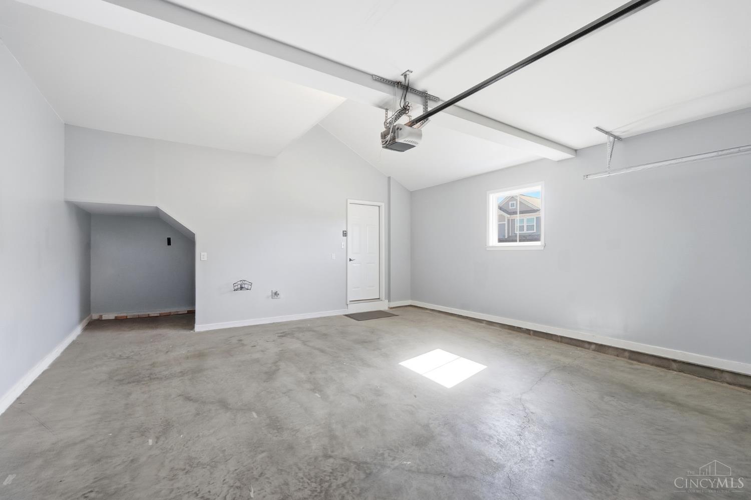 Empty garage with a concrete floor, ceiling-mounted opener, side door, and window.