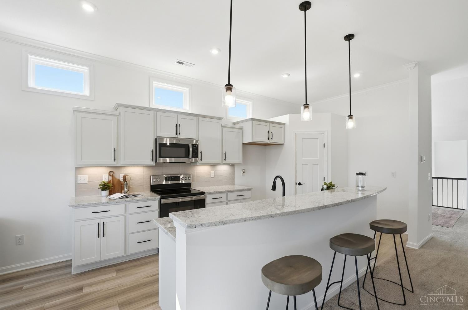 Bright white kitchen with a large granite island, three stools, and high windows.