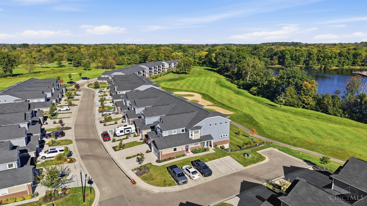 Aerial view of homes beside a golf course and wooded lake.