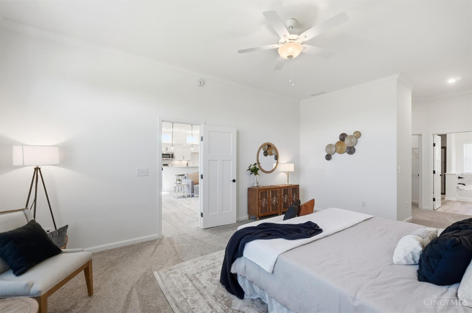 Furnished bedroom with a large bed, ceiling fan, and doorway to a bright kitchen.