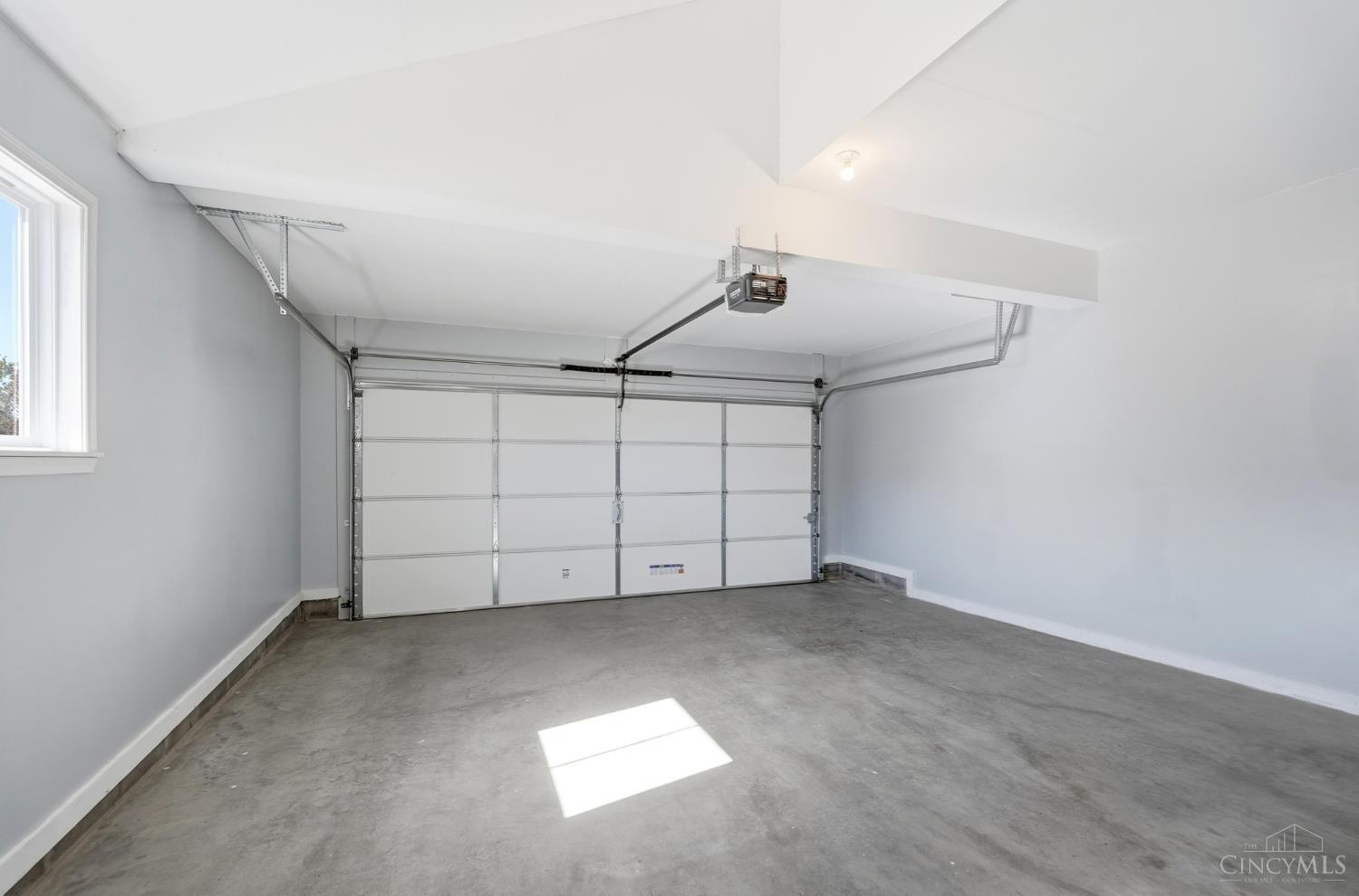 Empty garage with a concrete floor, overhead door, ceiling-mounted opener, and small window.