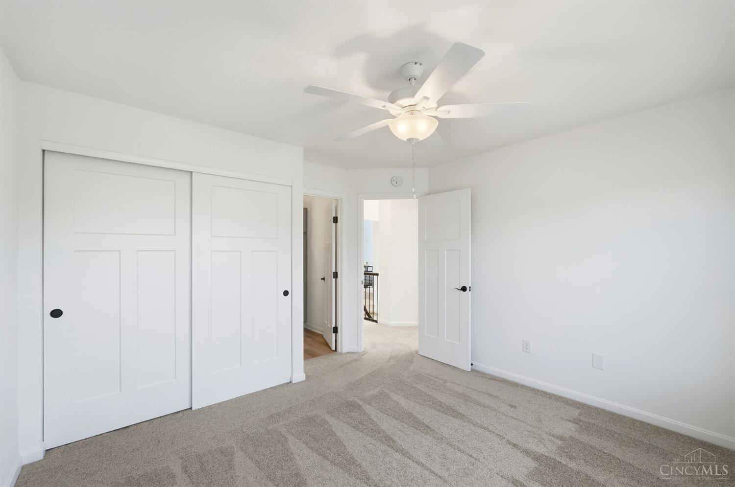 Empty bedroom with beige carpet, white sliding closet doors, and a ceiling fan with light.