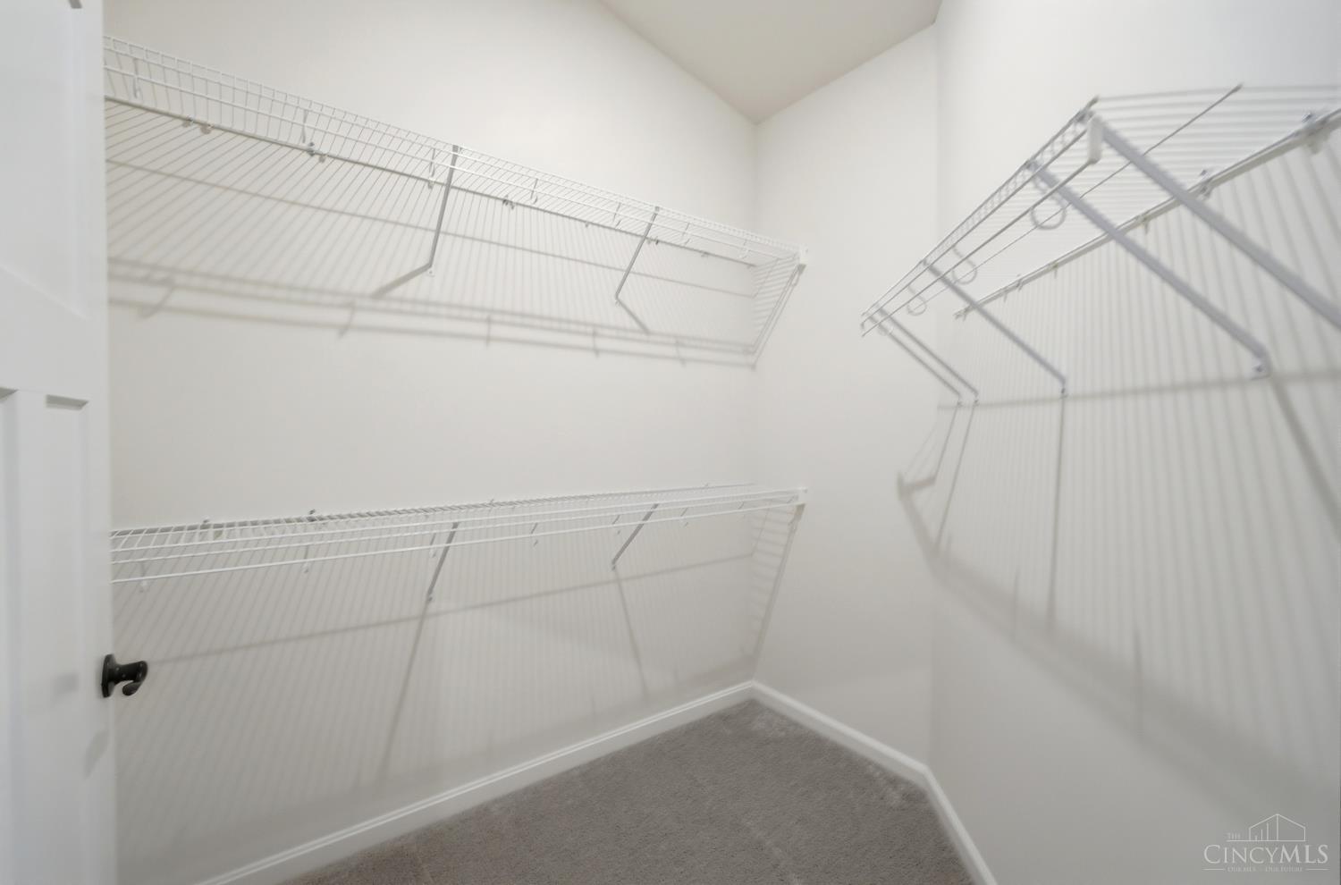 Walk-in closet with white wire shelving on three walls and gray carpet.