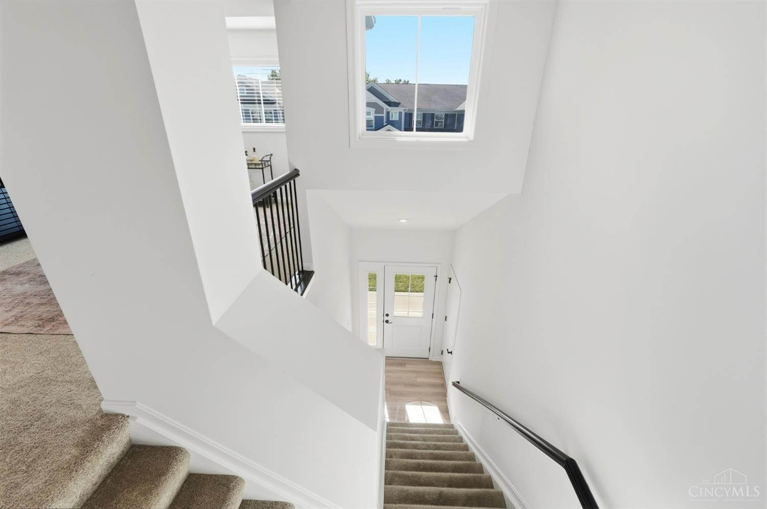 Carpeted staircase descends to a glass-paneled entry door beneath a large window.
