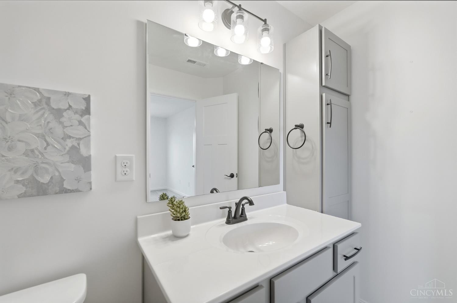 Bathroom vanity with a large mirror, white countertop, gray cabinetry, and a small succulent.