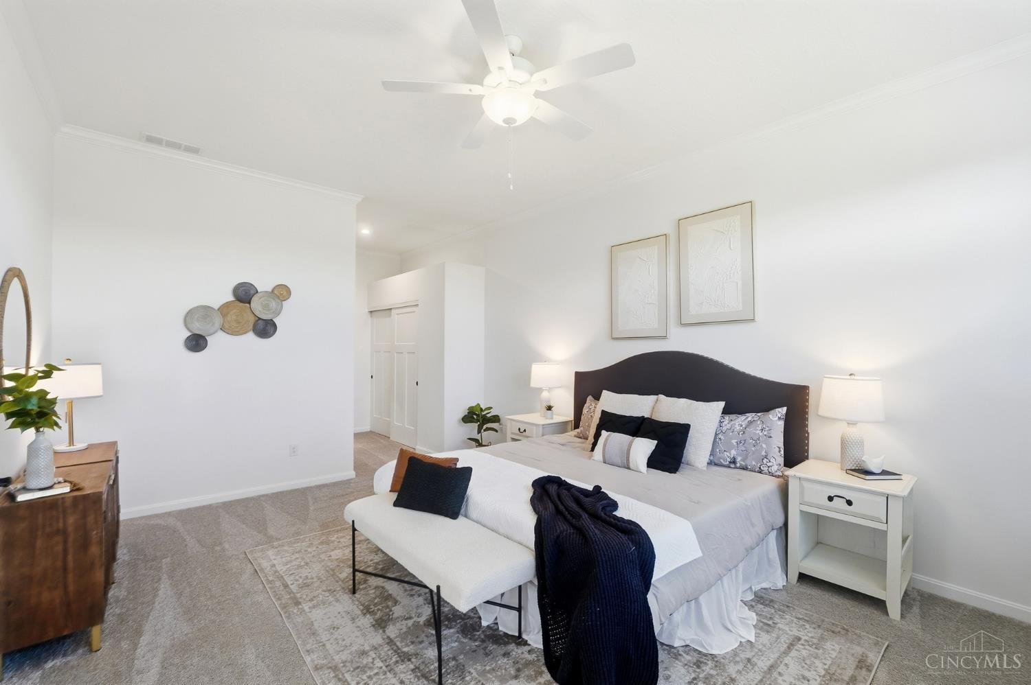 Staged bedroom with a dark curved headboard, layered bedding, and a white bench at the foot of the bed.