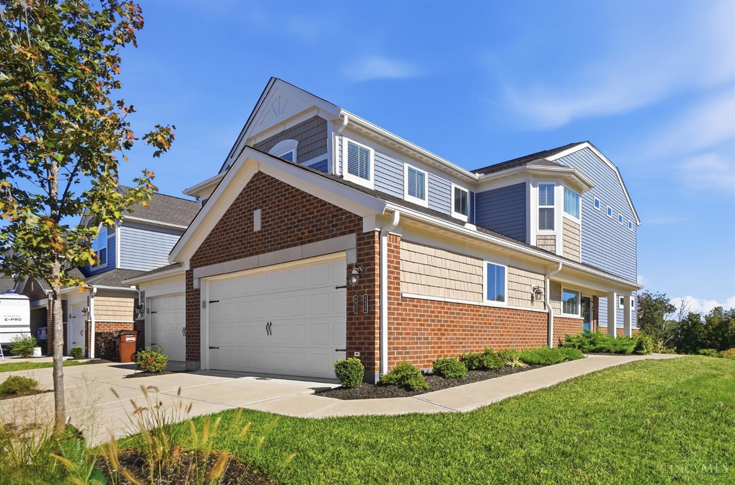 Two-story blue-gray and brick home with an attached double garage and autumn leaves in the foreground.