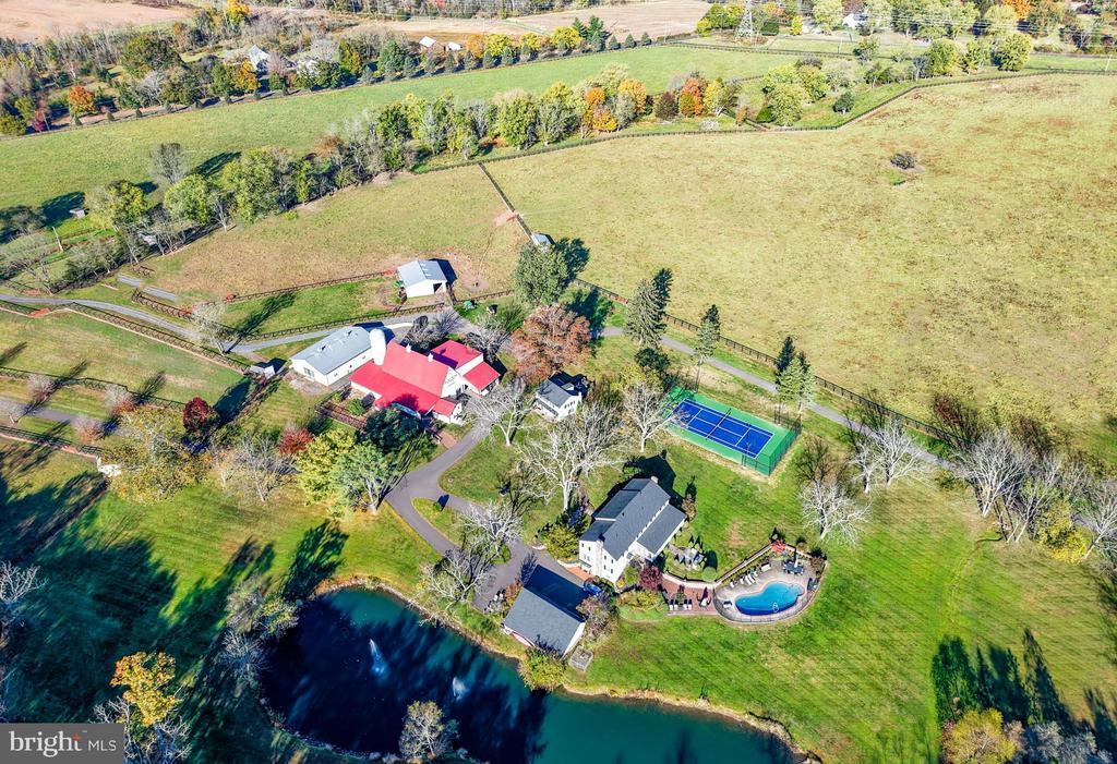Aerial view of an estate with open fields, a tennis court, pool, and pond.