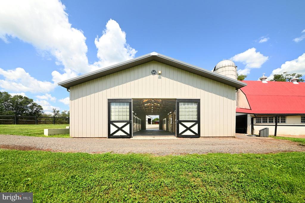 Light-colored barn with open double doors revealing a central aisle and stalls.