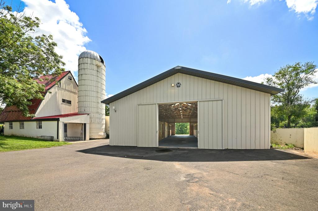 White open-front barn with an older red-roofed barn and silo behind it.