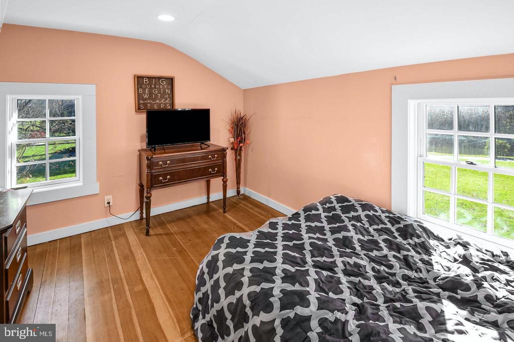 Bedroom with peach walls, hardwood floors, patterned bedding, and two windows overlooking a lawn.