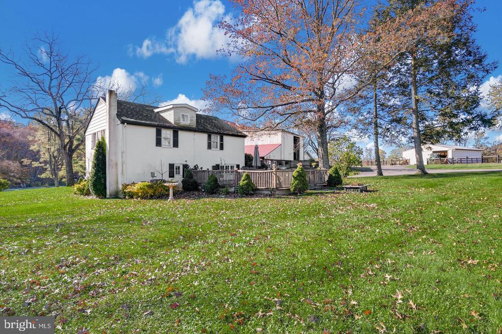 White farmhouse with a deck and expansive lawn, framed by autumn trees.