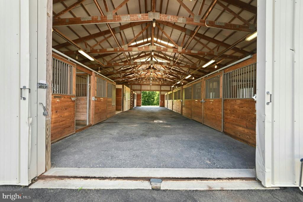 Horse stable aisle with wooden stalls on both sides and exposed timber roof trusses.