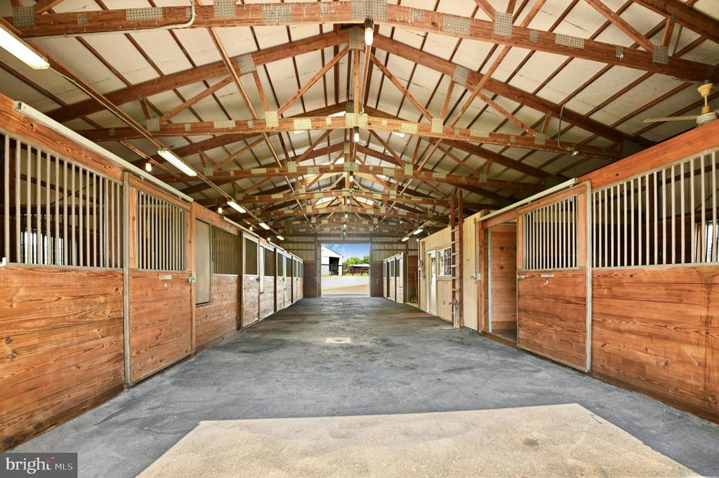 Horse barn aisle lined with wooden stalls beneath exposed timber trusses.