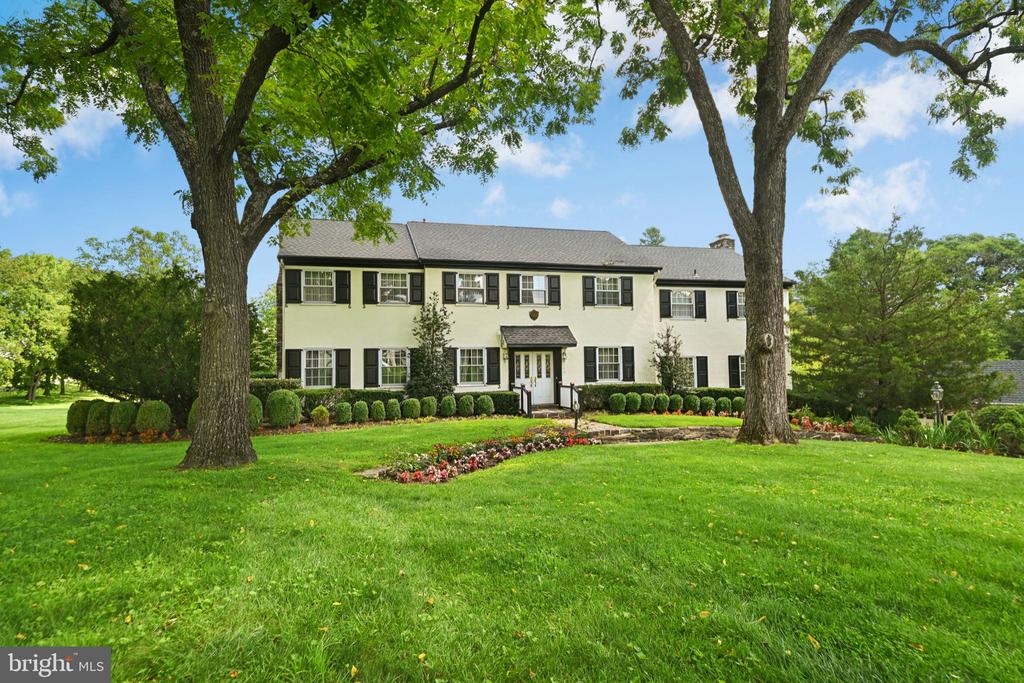 Two-story cream house with black shutters framed by mature trees and a landscaped lawn.
