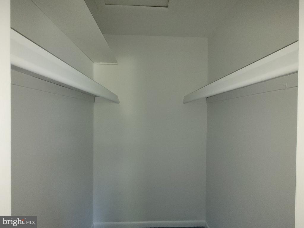 Empty walk-in closet with long shelves and hanging rods on both sides.