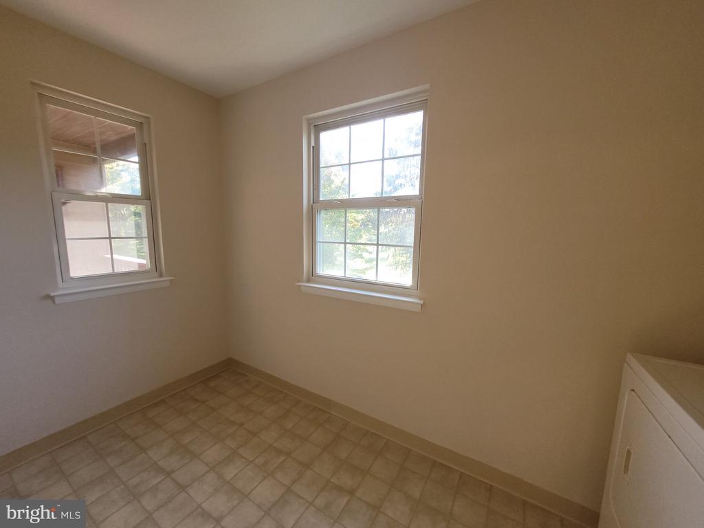 Small empty room with tiled floor, two windows, and a white appliance at the edge.